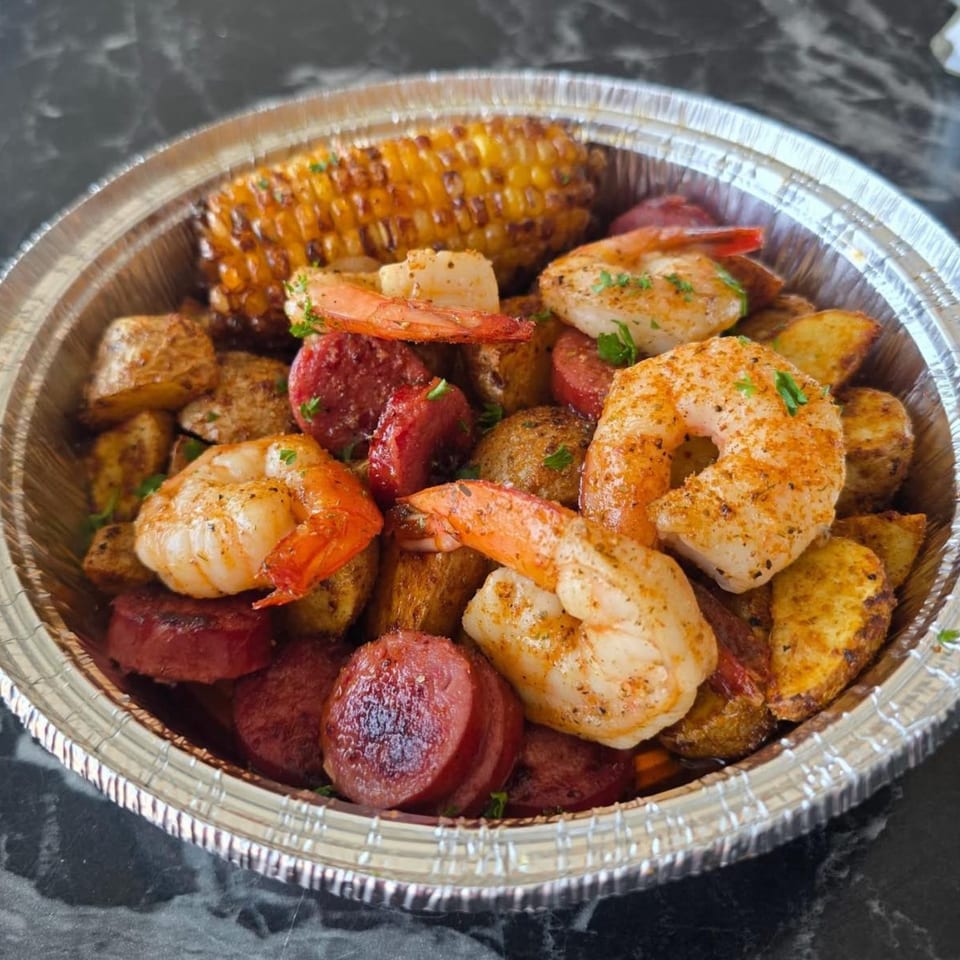 Men In The Kitchen's seafood boil with shrimp, sausage, potatoes, and corn in a foil container.