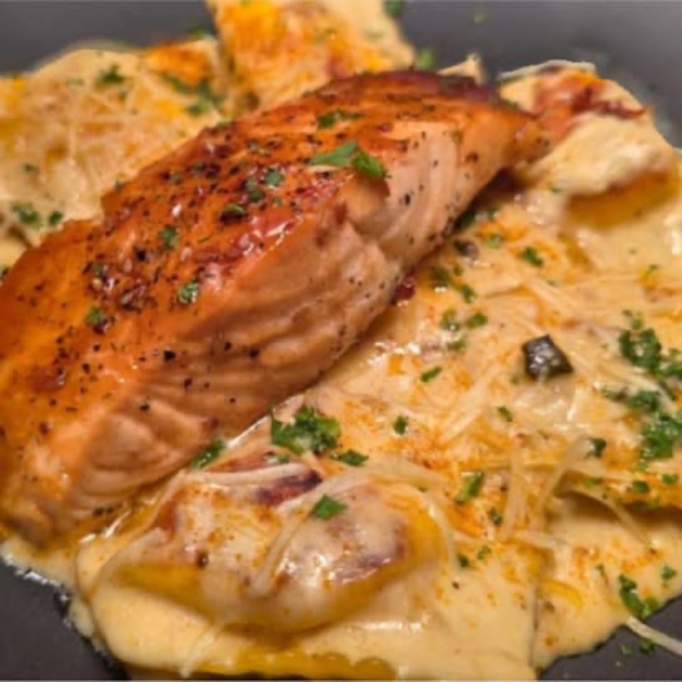Men In The Kitchen's pan-seared salmon with creamy ravioli, garnished with parsley and cheese.