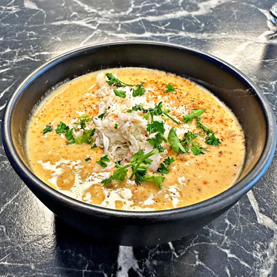 A bowl of creamy seafood bisque, topped with crab meat, fresh parsley, and spices.