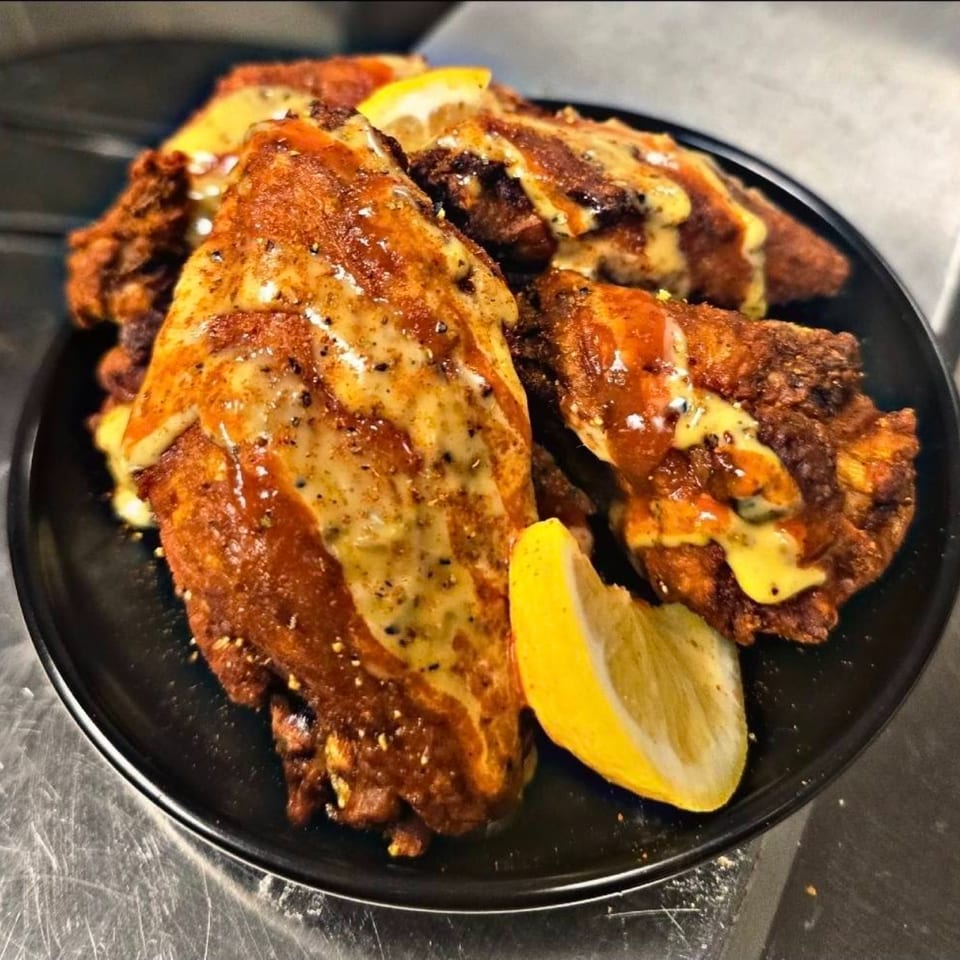 Close-up of golden-brown seafood, possibly fried fish or shrimp, drizzled with a creamy sauce and lemon wedges.