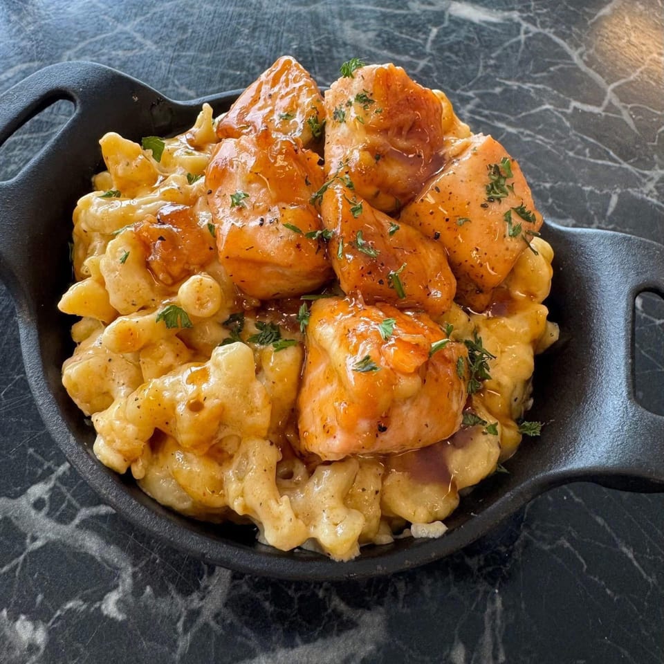 Seafood mac and cheese with large pieces of salmon, garnished with herbs in a black skillet.